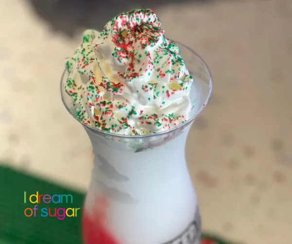 Close-up of a white ice cream topped with a tall swirl of whipped cream and red and green sprinkles.